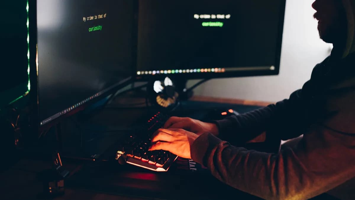 Side view of crop anonymous male cyber thief accessing information on desktop computer screens at dusk