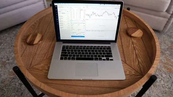 Close-up of a laptop displaying trading charts on a stylish wooden table, ideal for financial themes.