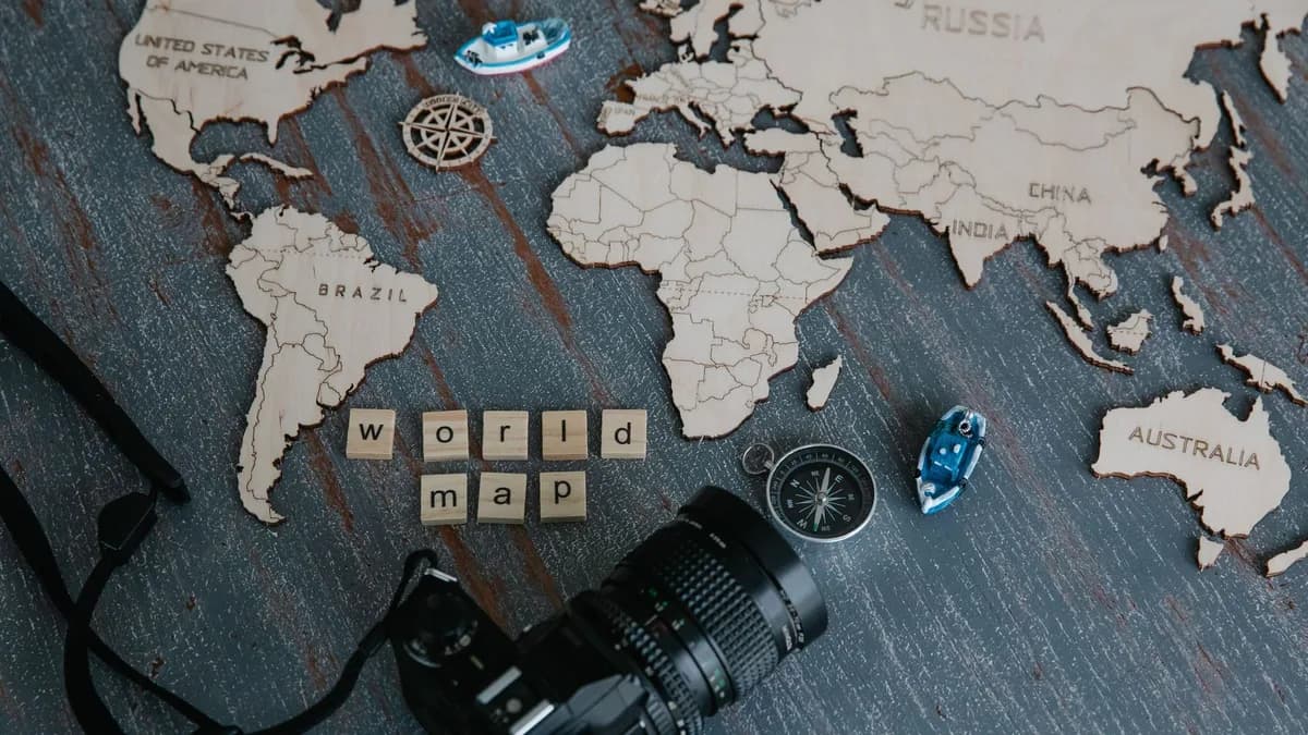 A creative flat lay of a wooden world map, camera, and compass.