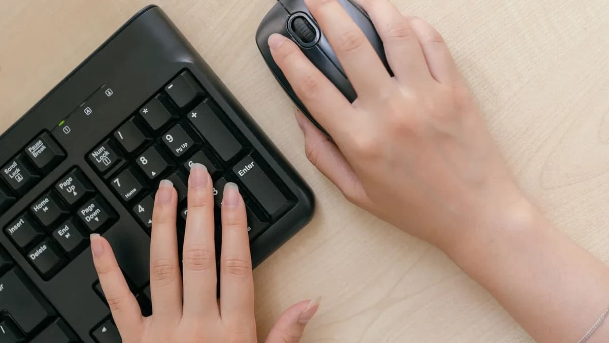 Close-up of hands on a keyboard and mouse, highlighting office work setup.