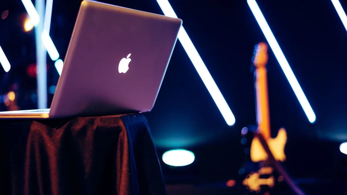 A sleek laptop sits on a table with vibrant neon lights and a guitar in the background.