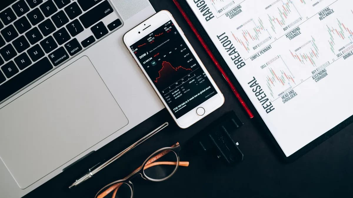 Top view of financial tools including a laptop, smartphone with stock data, and charts for market analysis.