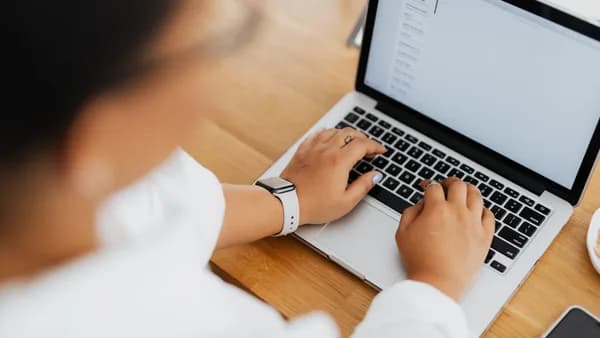 High angle shot of a person typing on a laptop, focused on hands and keyboard.