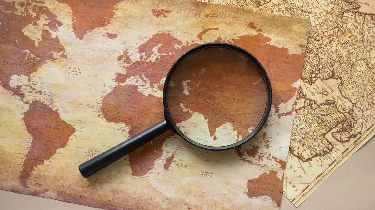 A top view of a vintage world map with a magnifying glass highlighting regions for exploration.