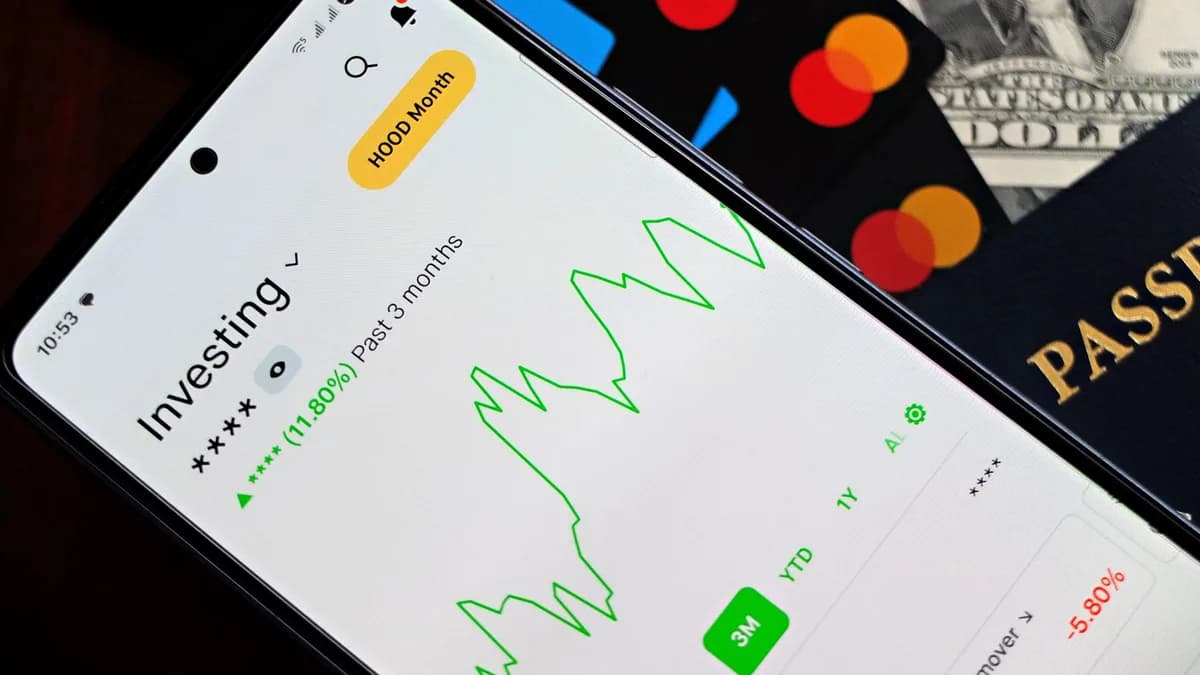 A smartphone showing an investment app with green growth indicators, surrounded by credit cards, US dollars, and a passport.