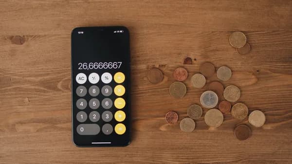 Overhead view of a smartphone calculator with European coins on a wooden surface, symbolizing modern finance.