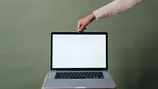 A hand holding open a laptop with a blank screen against a green background, ideal for mockup use.
