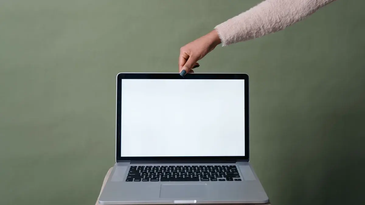 A hand holding open a laptop with a blank screen against a green background, ideal for mockup use.