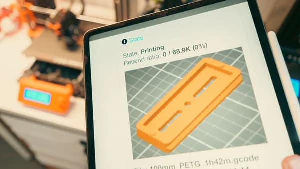 Close-up of a digital tablet displaying a 3D printing process in a workshop setting.