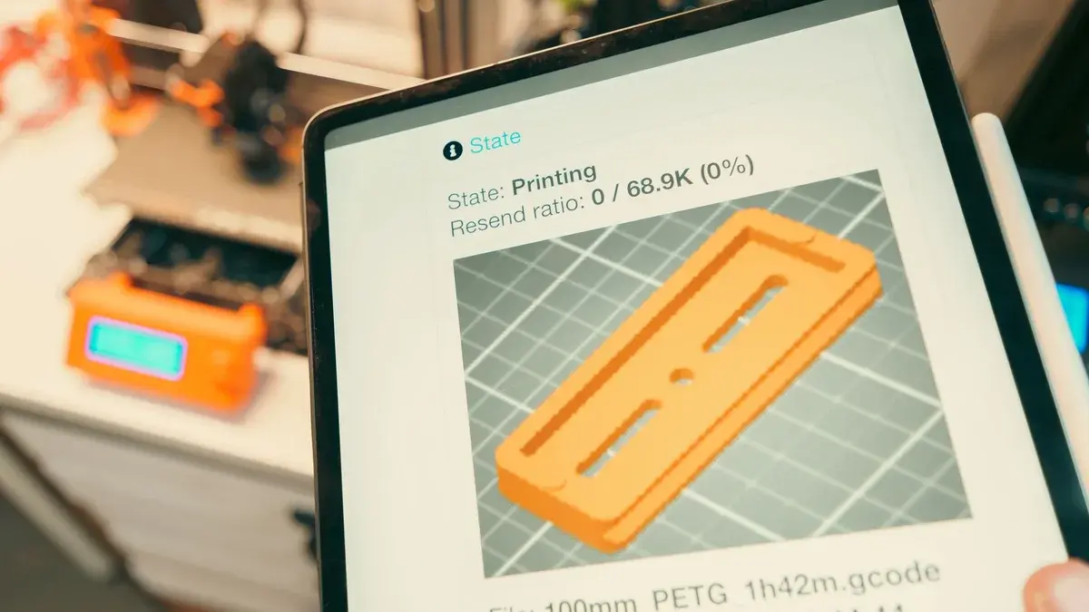 Close-up of a digital tablet displaying a 3D printing process in a workshop setting.