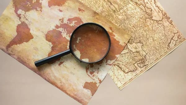 Top view of round black magnifying glass placed on paper maps with continents on beige background in light modern room