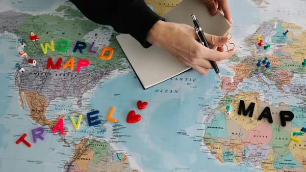 Hands holding pen and notebook over vibrant world map planning a journey.