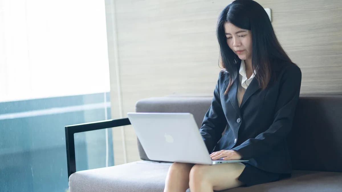 Asian businesswoman in smart casual attire working on laptop in a modern office setting.