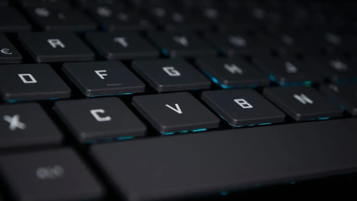 A close-up shot of a backlit keyboard in a dark setting, highlighting the keys.