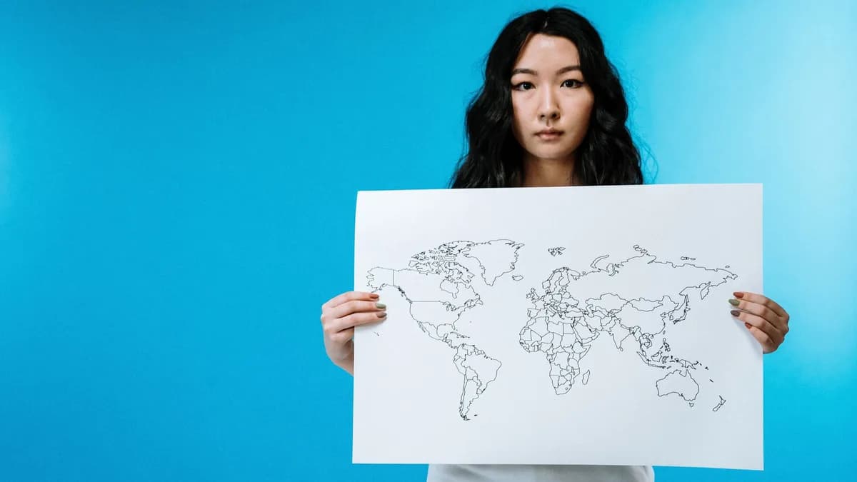 Portrait of a young woman holding a world map against a vivid blue background.