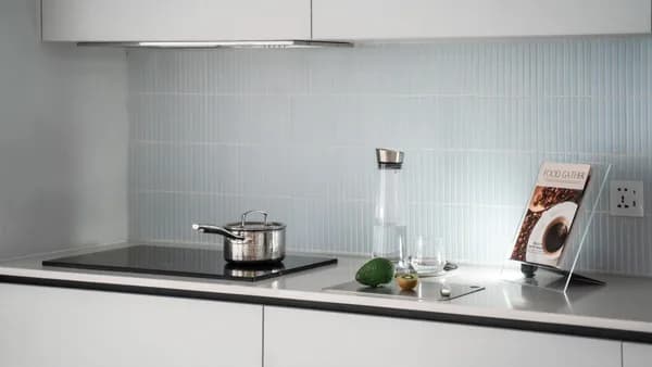 Elegant minimalist kitchen counter with induction stove, pot, glassware, and cookbook.