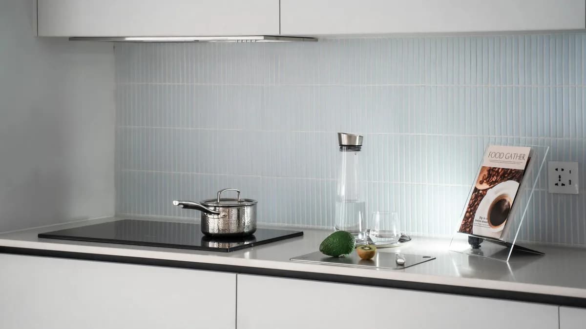 Elegant minimalist kitchen counter with induction stove, pot, glassware, and cookbook.