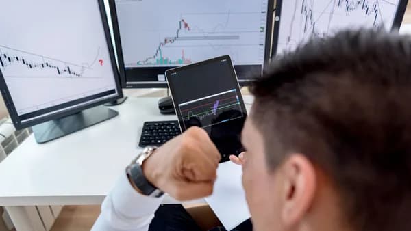 A trader confidently viewing stock market charts on multiple monitors in a modern workspace.