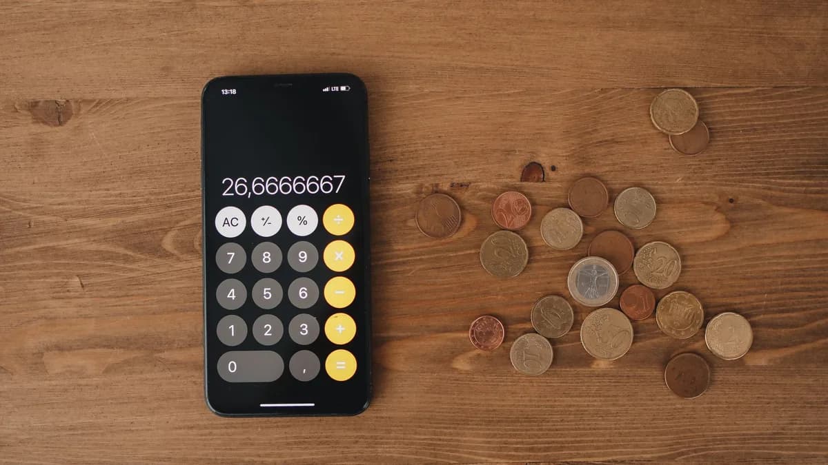 Overhead view of a smartphone calculator with European coins on a wooden surface, symbolizing modern finance.