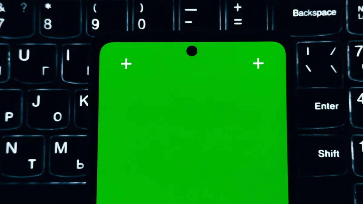 A close-up of a smartphone with a green screen placed on a laptop keyboard.