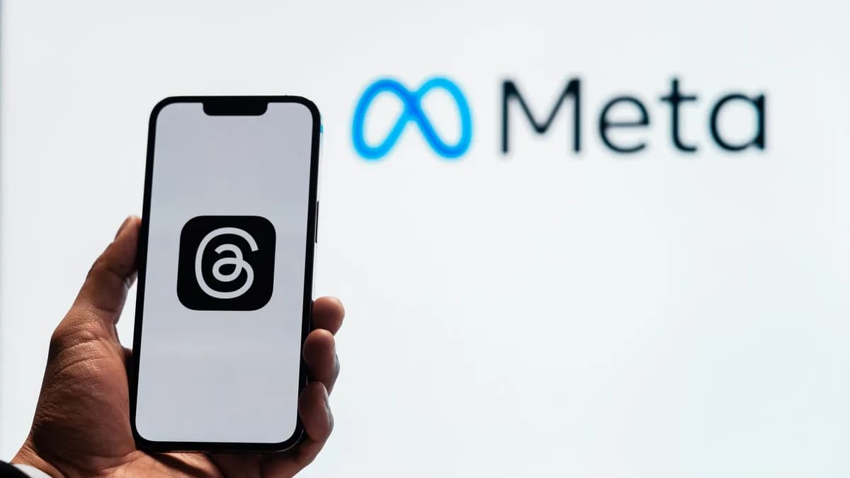 A hand holding a smartphone showing the Threads app with Meta logo in the background.