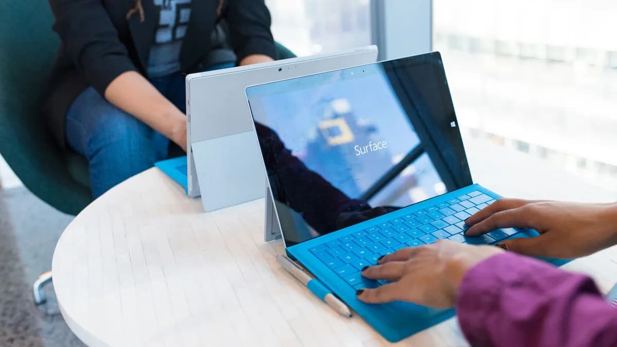 Two people using modern laptops in a bright office setting, showcasing technology in use.