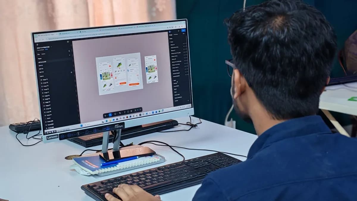 A young designer focused on creating user interfaces on a desktop computer in an office setting.