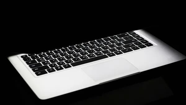 A modern laptop with a glowing keyboard illuminated in a dark, minimalist setting.