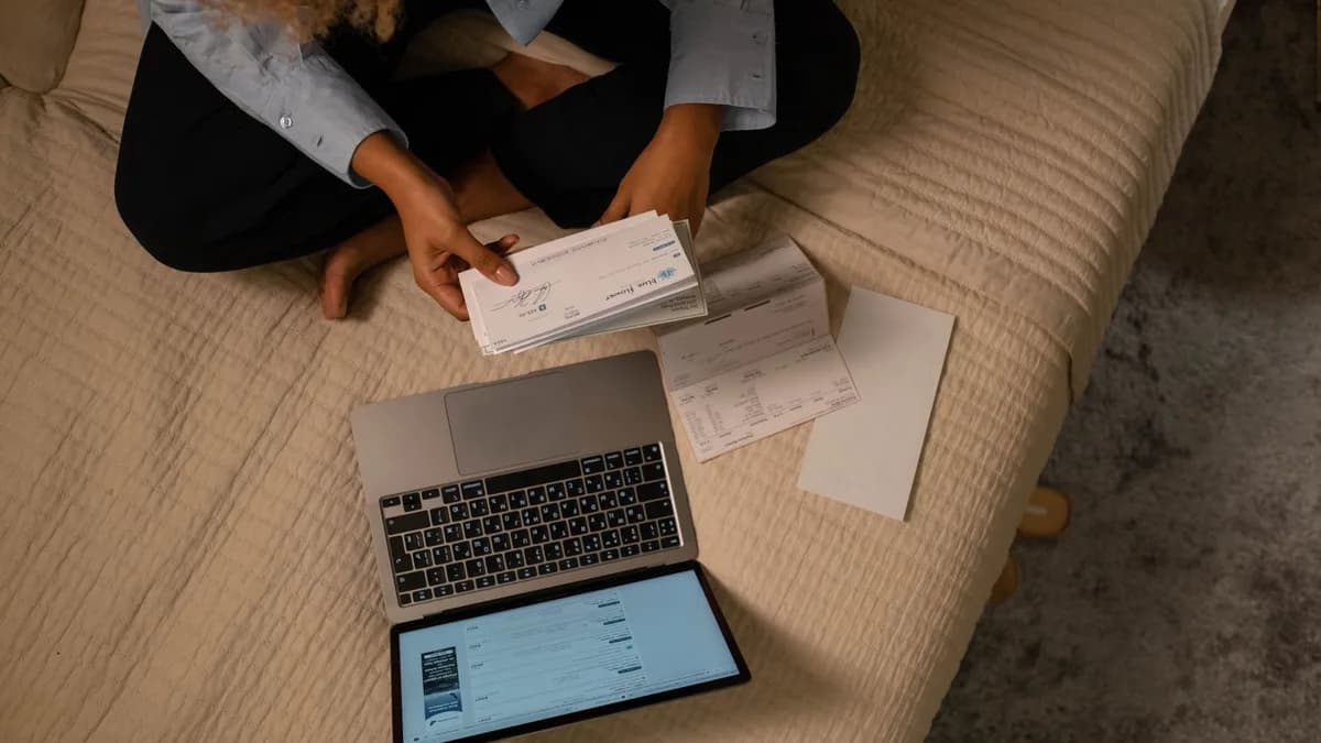Overhead view of woman organizing finances on bed with laptop and checks.