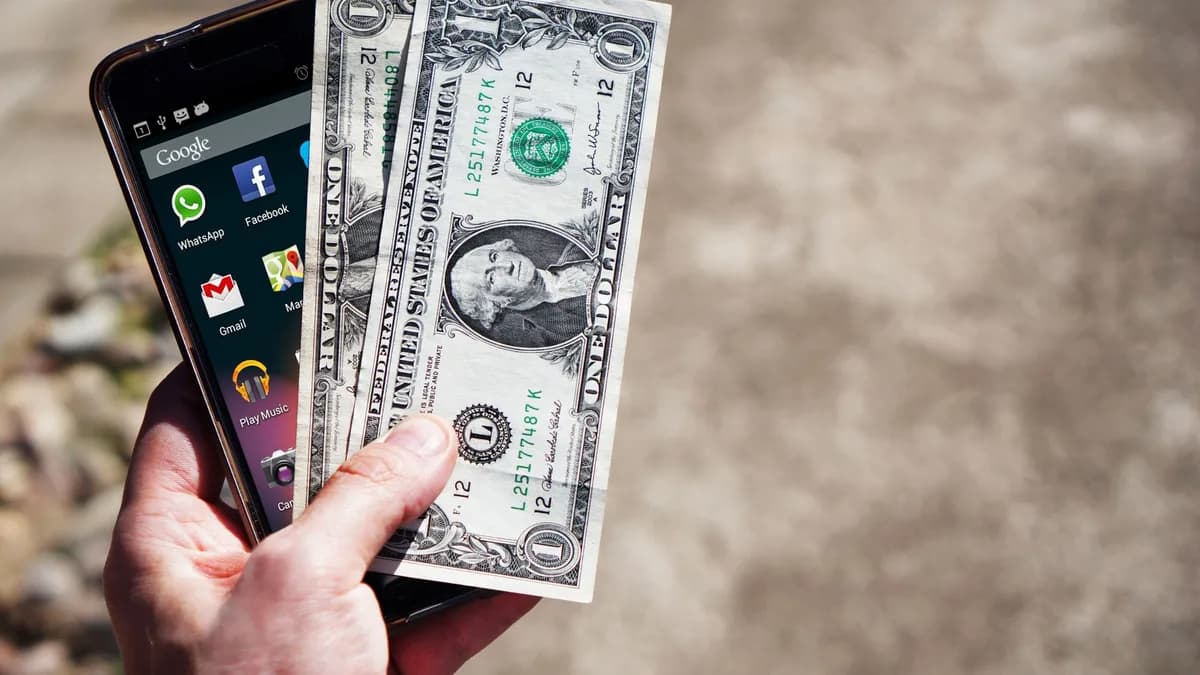 Close-up of a hand holding US dollar bills and a smartphone outdoors, showcasing financial technology.