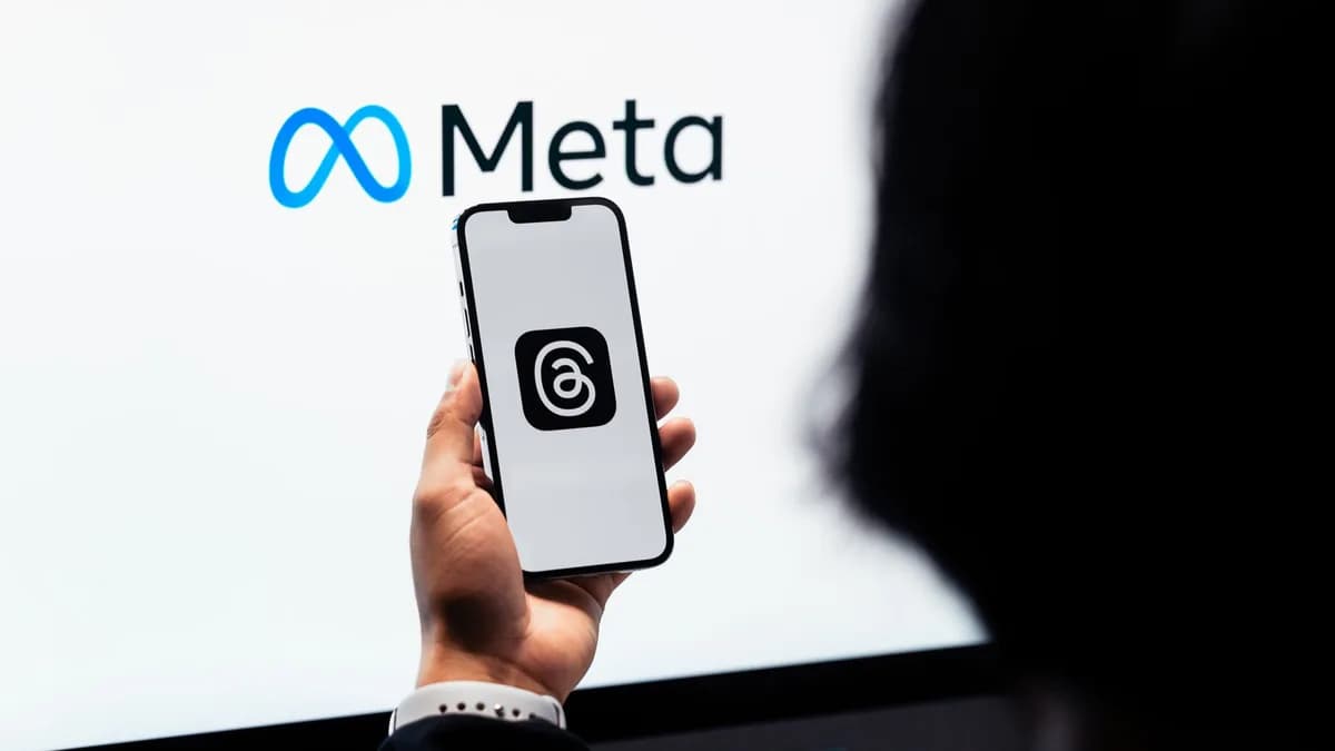 Hands holding smartphone with Meta Threads logo on screen, Meta branding in background.