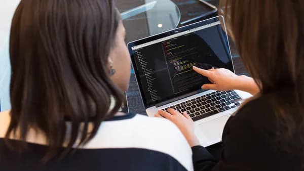 Two women working together on software programming indoors, focusing on code.