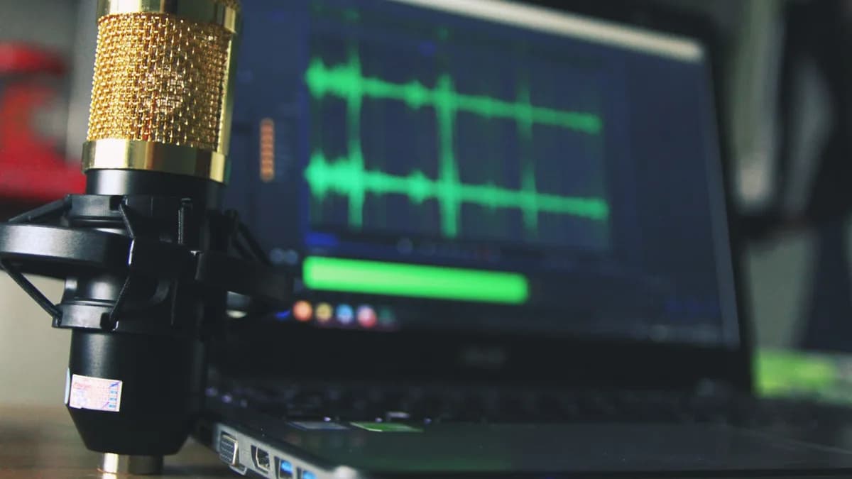 Close-up of a golden microphone and laptop used for audio editing.