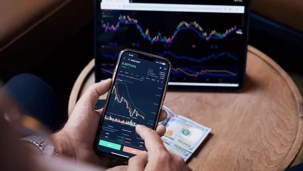 Close-up of a person trading stocks using a smartphone and a tablet.