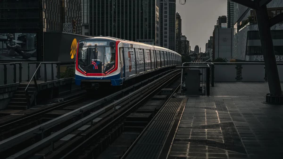 A modern train travels on an elevated track amid city skyscrapers at twilight.