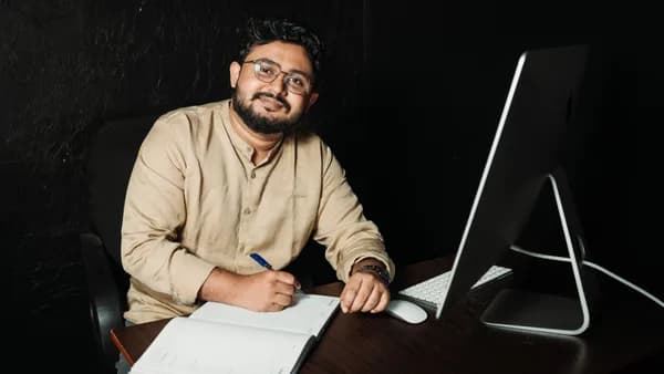 A man with a beard working at a desk with a computer and notebook, showcasing modern office life.