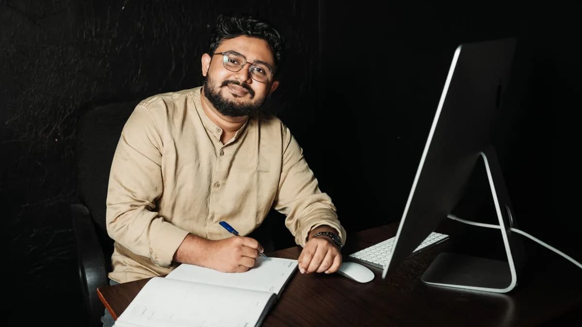 A man with a beard working at a desk with a computer and notebook, showcasing modern office life.