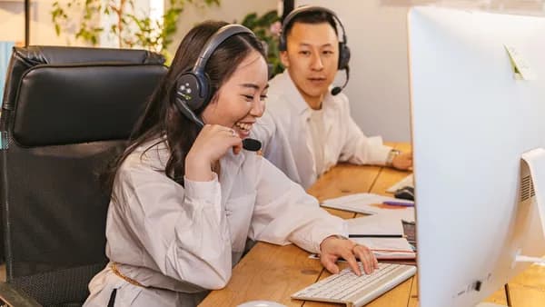 Two call center agents working together, focused and engaged at their desks, communicating via headsets.