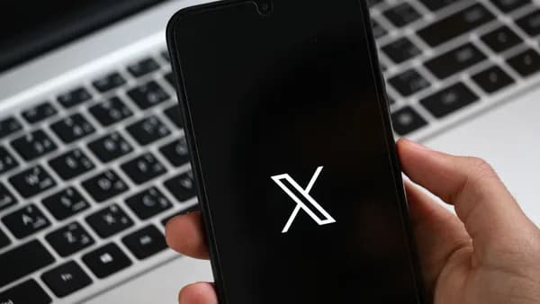 A hand holds a smartphone displaying a modern app interface, with a laptop keyboard in the background.