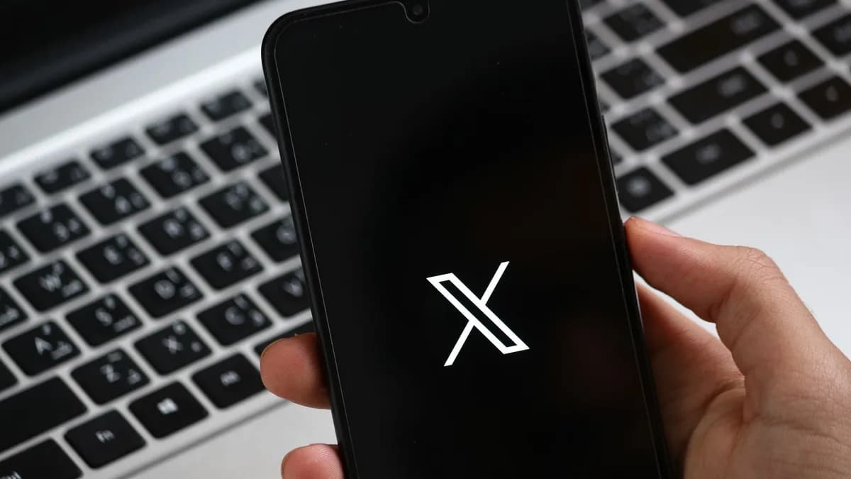 A hand holds a smartphone displaying a modern app interface, with a laptop keyboard in the background.
