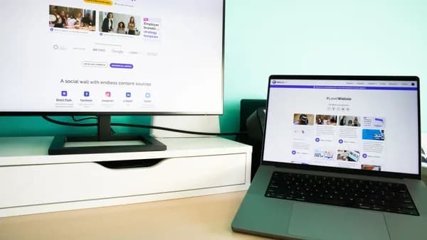 Office desk workspace with a laptop and a monitor displaying a social media wall solution.