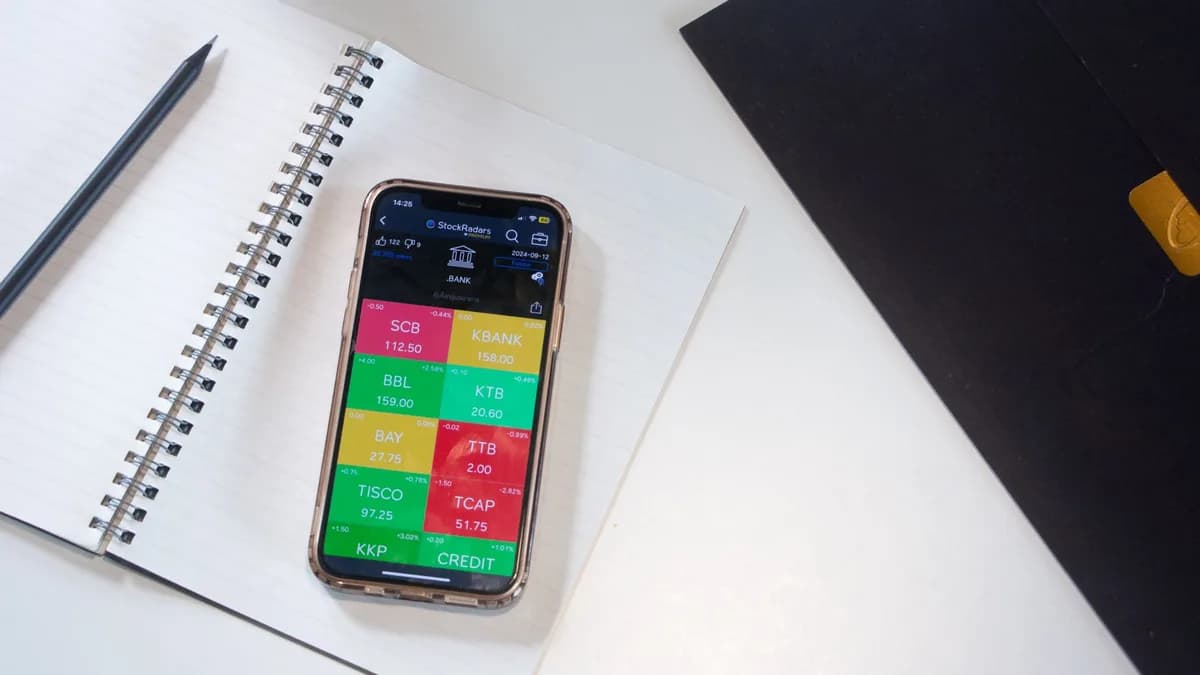A smartphone displays a financial stock market app on a desk with a notebook and pencil.