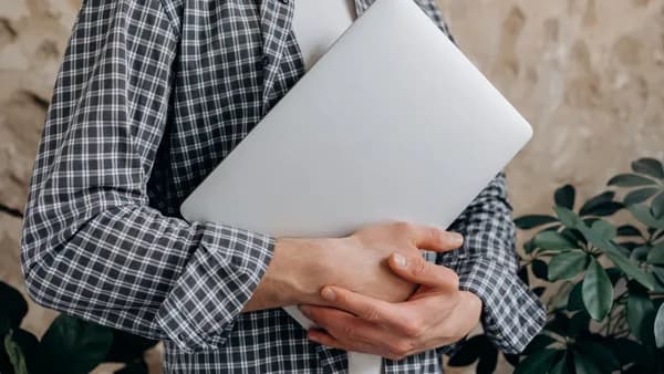 Close-up of a young adult casually holding a laptop indoors, showcasing modern freelance lifestyle.