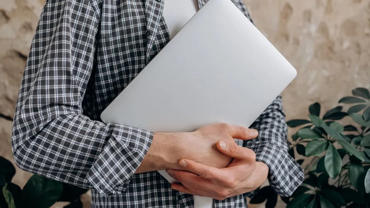 Close-up of a young adult casually holding a laptop indoors, showcasing modern freelance lifestyle.