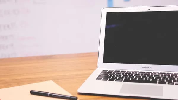 Sleek laptop on wooden desk with pen and notepad, ideal for business and tech settings.