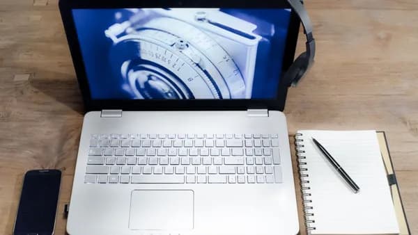Top view of a modern workspace with a laptop, smartphone, headphones, and a notebook on a wooden desk.