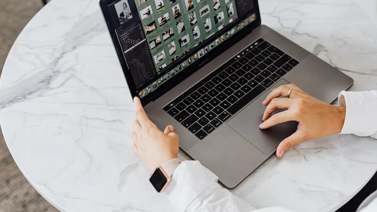 Hands editing photos on laptop, modern workspace on marble table.