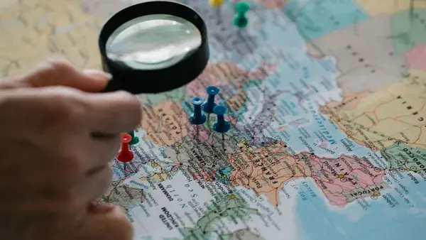 Magnifying glass focuses on pins highlighting travel destinations on a world map.
