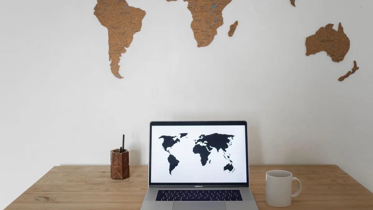 Black world map on laptop screen and ceramic cup with pen container placed on table against silhouettes of continents