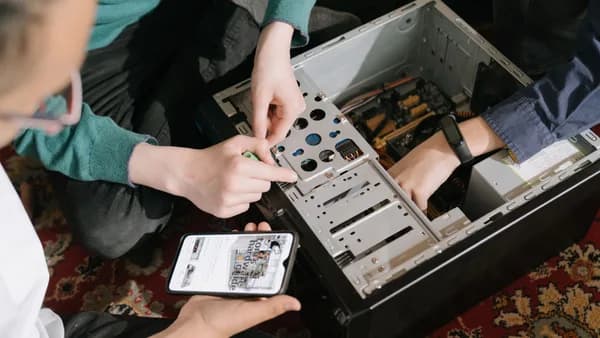 A close-up of hands fixing a computer with guidance from a mobile device.